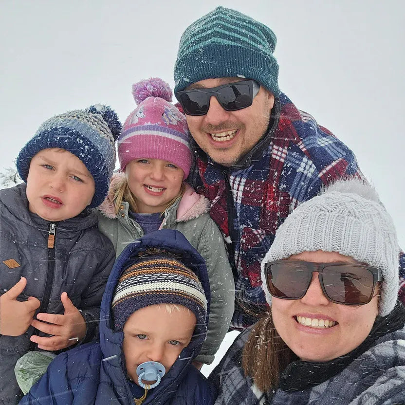 Family of five posing together in snowy weather, wearing winter clothing and sunglasses.